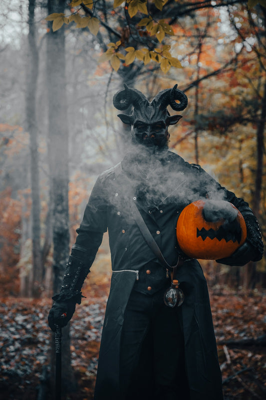 Horned figure holds smoking halloween pumpkin in autumn forest