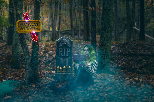 Spooky figure reads by a tombstone in a misty forest